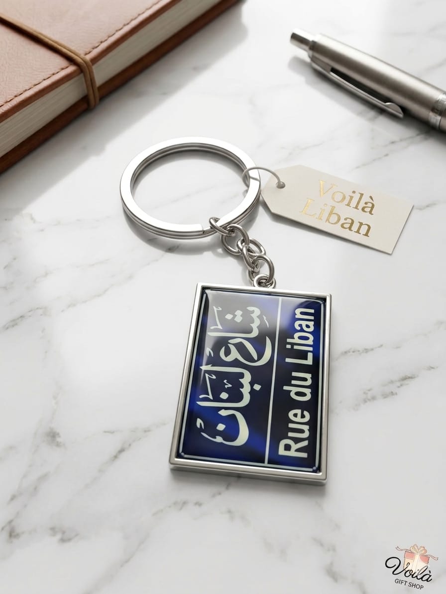 Keychain with 'Rue du Liban' design on a marble surface with a notebook and pen.