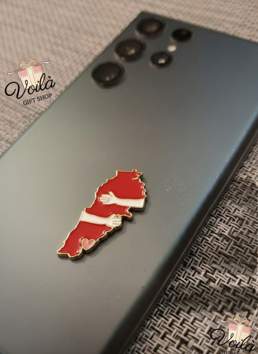 Red and white map-shaped pin on a dark phone case with 'Voila Gift Shop' branding.