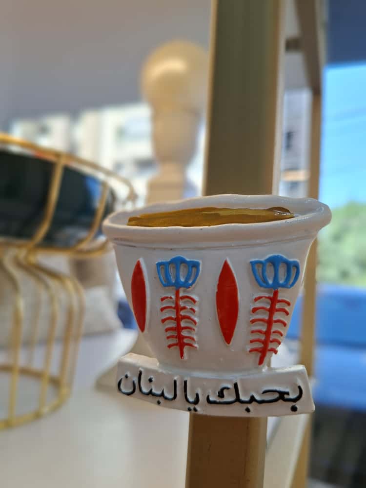 Small decorative pot with floral designs and Arabic text on a blurred background