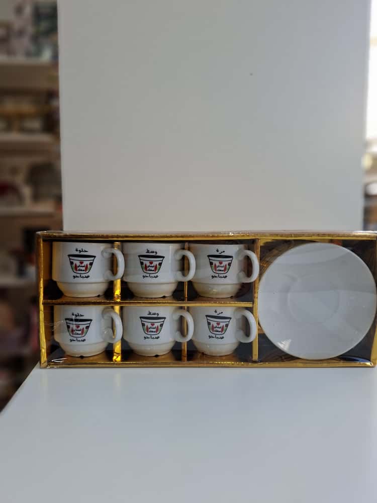 Set of six white coffee cups with a logo in a gold box on a white surface.