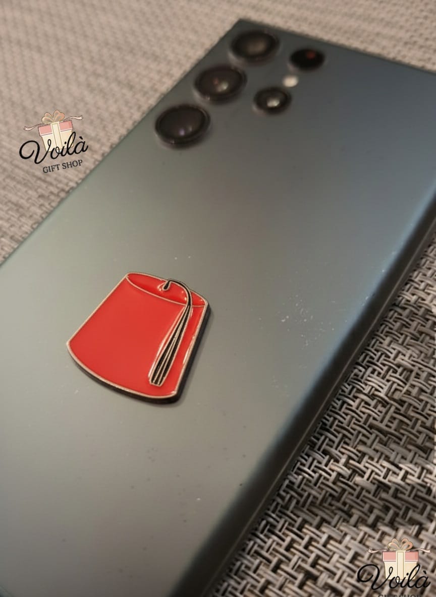 Red tag pin on a phone case with 'Voila' branding.