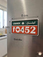 Red and green decorative Lebanese license plate fridge magnet measuring 8cm by 4cm, displaying the patriotic number 10452 with a heart, the national Cedar tree, and the white silhouette of the Lebanon map, placed on a stainless steel refrigerator.
