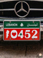 Red and green decorative Lebanese license plate mounted on a classic car, prominently displaying the patriotic number 10452 with a heart, the national Cedar tree, and the white silhouette of the Lebanon map.