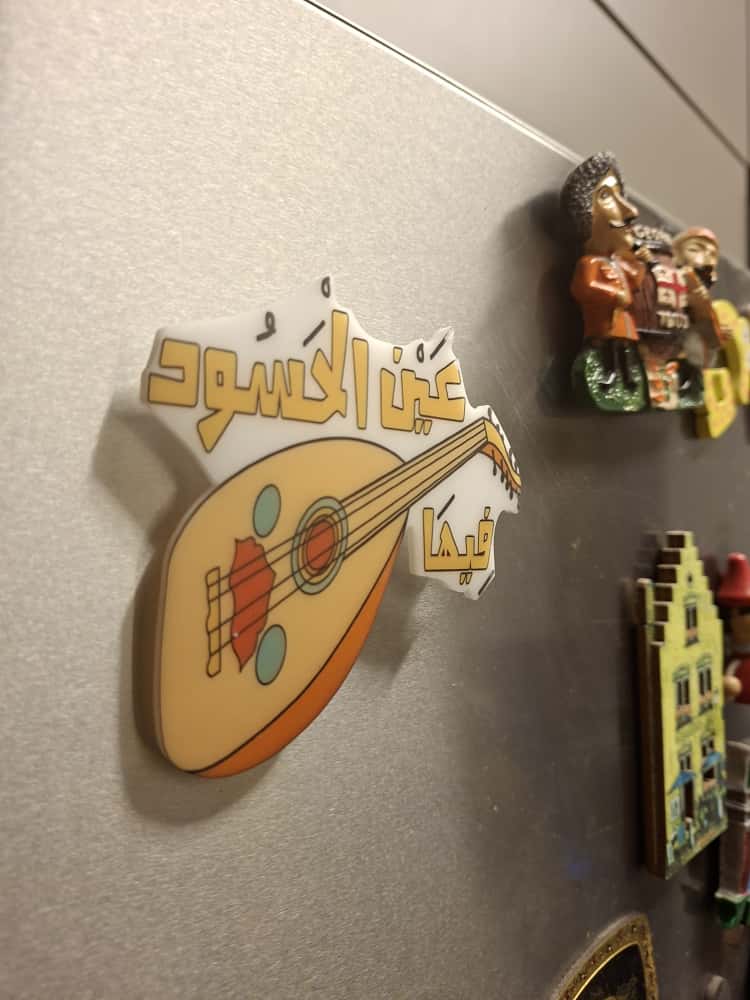 Fridge magnet with a lute design and Arabic text on a metallic surface.