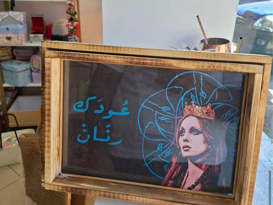 Decorative screen with a stylized portrait and Arabic text in a wooden frame.