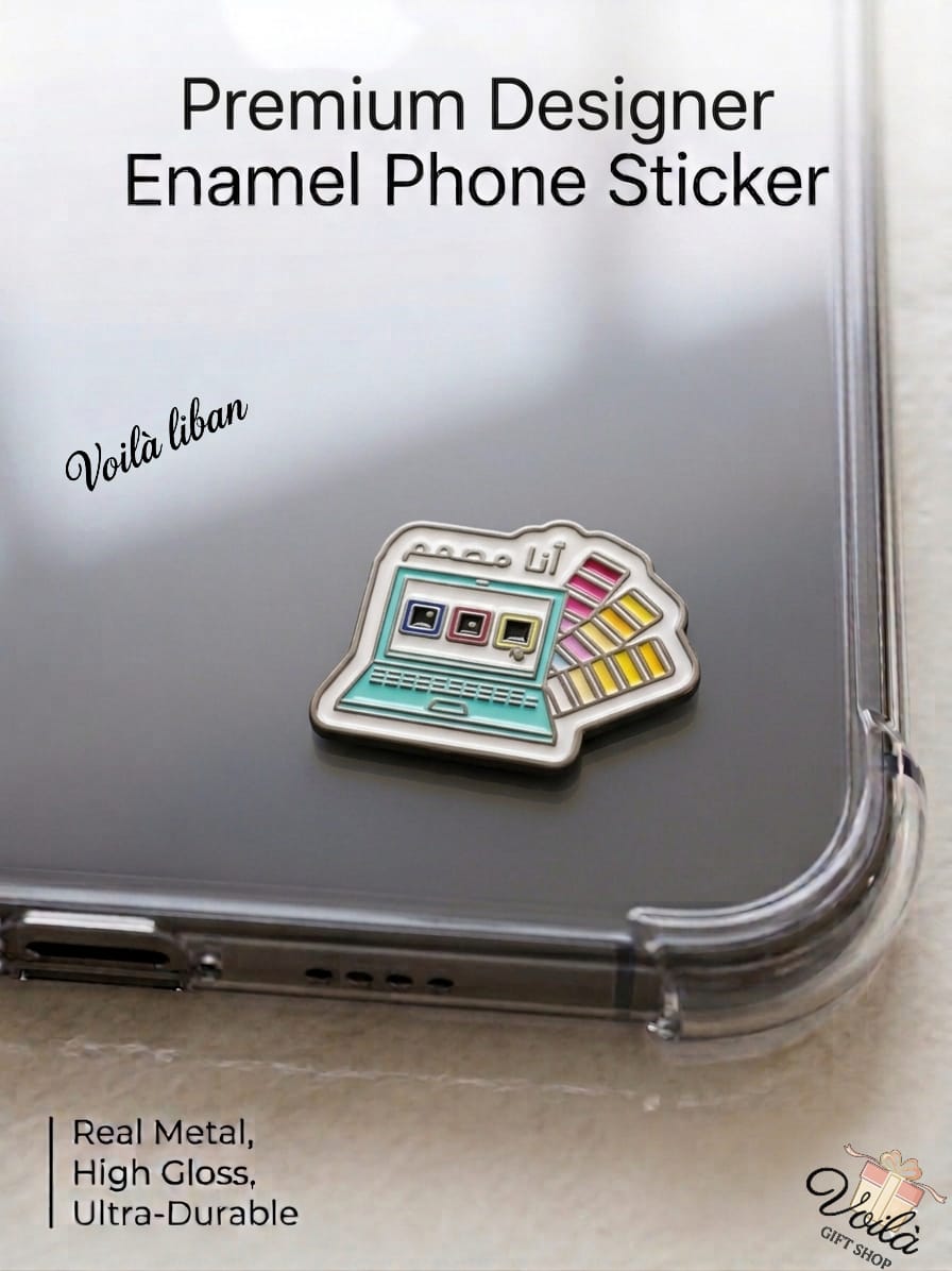 Premium metal enamel phone sticker shaped like a vintage teal laptop displaying design software on the screen alongside a colorful Pantone-style swatch fan, featuring the Arabic phrase "أنا مصمم" written above the laptop screen, attached to a clear phone case.