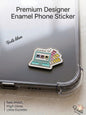 Premium metal enamel phone sticker shaped like a vintage teal laptop displaying design software on the screen alongside a colorful Pantone-style swatch fan, featuring the Arabic phrase "أنا مصمم" written above the laptop screen, attached to a clear phone case.