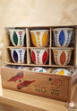 Set of six colorful ceramic cups in a wooden box with decorative patterns.