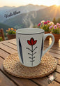 Steaming mug with floral design on a woven coaster, set against a scenic backdrop with mountains and flowers.