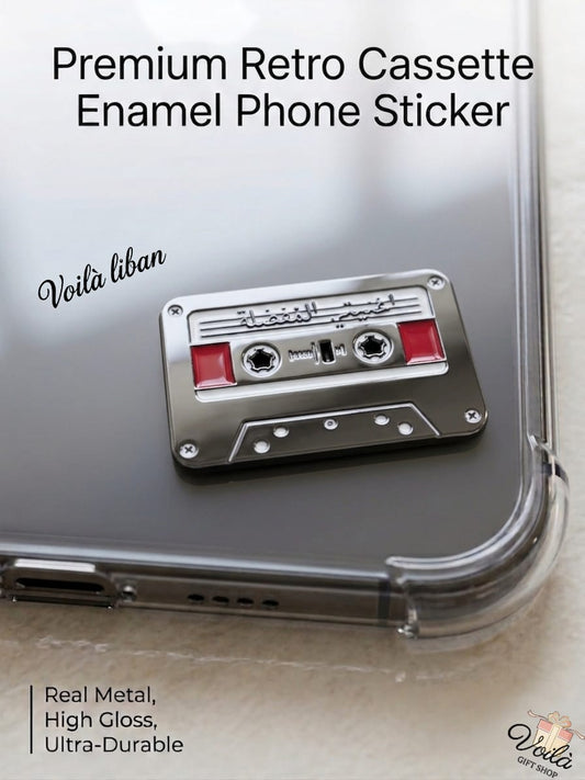 Premium silver metal enamel phone sticker shaped like a retro cassette tape with red accents, featuring the handwritten Arabic phrase "أغنيتي المفضلة" (My Favorite Song) on the label, attached to a clear phone case.