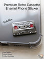 Premium silver metal enamel phone sticker shaped like a retro cassette tape with red accents, featuring the handwritten Arabic phrase "أغنيتي المفضلة" (My Favorite Song) on the label, attached to a clear phone case.