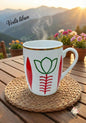 White mug with red and green design on a woven coaster, set against a scenic mountain backdrop with 'Voila Liban' text.