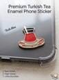 Premium metal enamel phone sticker shaped like a traditional Turkish tea glass (Istikan) filled with red tea on a gold saucer with red accents, featuring a small gold spoon, attached to a clear phone case.