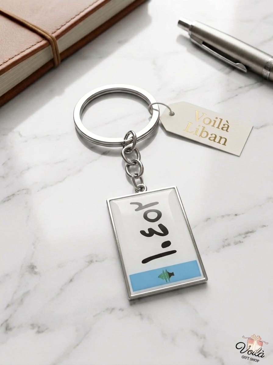 Keychain with a small book design on a marble surface with a pen and notebook.