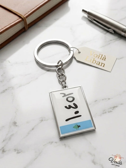 Keychain with a small book design on a marble surface with a pen and notebook.