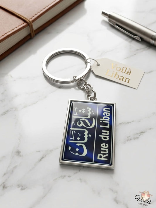 Keychain with 'Rue du Liban' design on a marble surface with a notebook and pen.