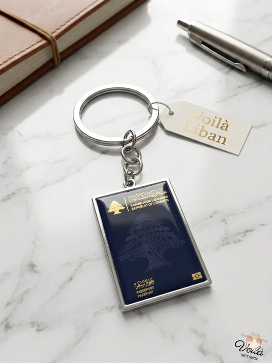 Keychain shaped like a lebanese passport on a marble surface with a pen and notebook.