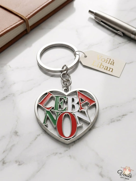 Heart-shaped keychain with 'Lebanon' in red and green on a marble surface with a notebook and pen.