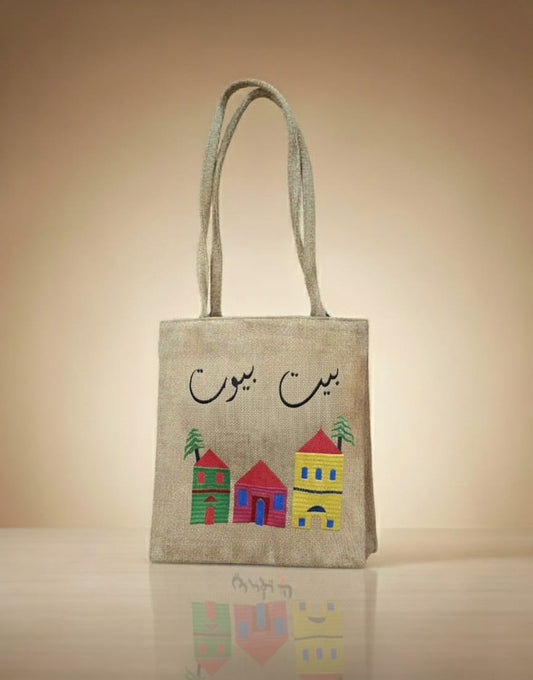 Jute bag with colorful house illustrations and Arabic text on a beige background
