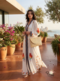 Elegant white embroidered kaftan with parrot print and woven straw bag overlooking Beirut coast