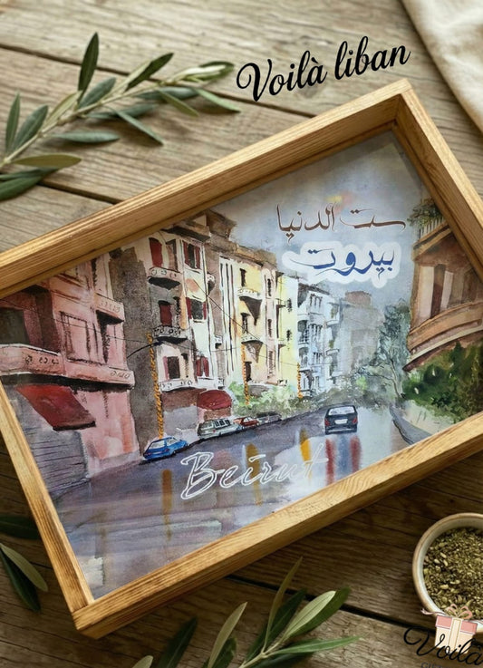 Framed artwork of a city street with 'Beirut' written on it, placed on a wooden surface.