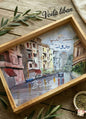 Framed artwork of a city street with 'Beirut' written on it, placed on a wooden surface.
