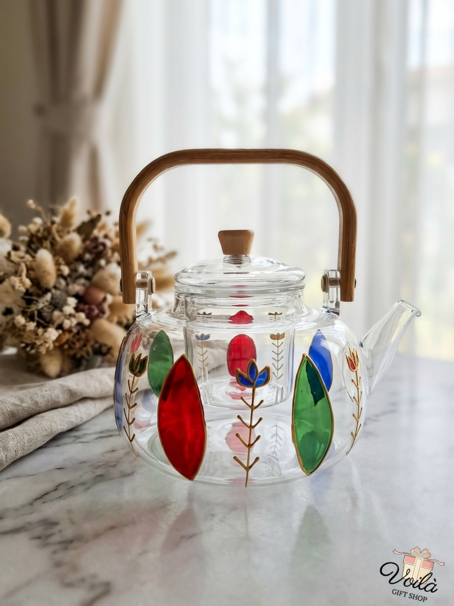 Hand-painted glass teapot with colorful motifs and a bamboo handle on a marble table