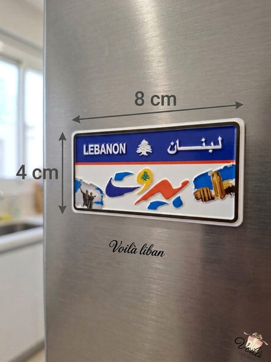 Decorative Beirut Lebanon license plate fridge magnet measuring 8cm by 4cm, featuring the Lebanese cedar, stylized Beirut Arabic text, Raouche Rocks, and Martyrs' Monument, placed on a stainless steel refrigerator.