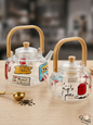 Two hand-painted glass teapots with bamboo handles featuring Lebanese cultural phrases and symbols