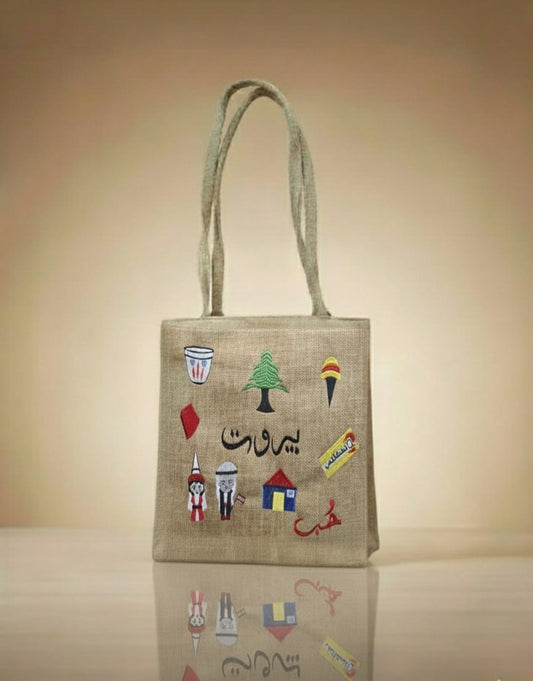 Jute bag with colorful embroidered designs on a reflective surface with a beige background