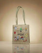 Jute bag with colorful embroidered designs on a reflective surface with a beige background