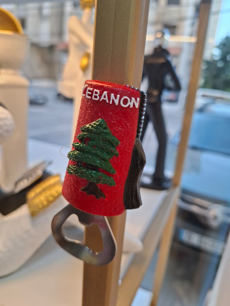 Red bottle opener with 'Lebanon' text and tree design on a blurred street background