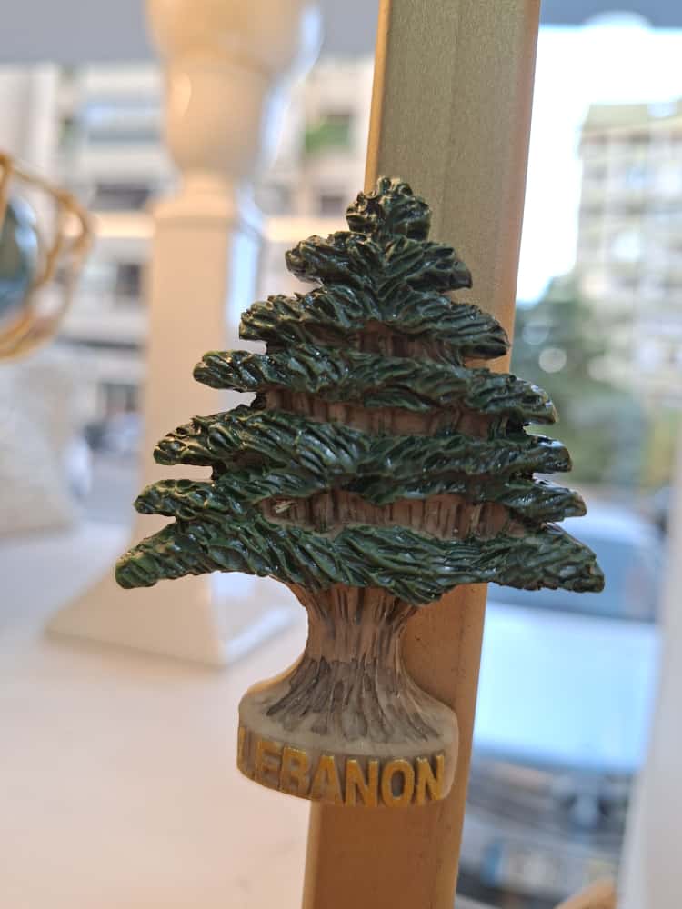 Decorative bottle stopper shaped like a pine tree with 'Lebanon' text on a blurred background