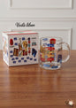 Clear glass mug with colorful designs on a wooden surface next to its packaging box.