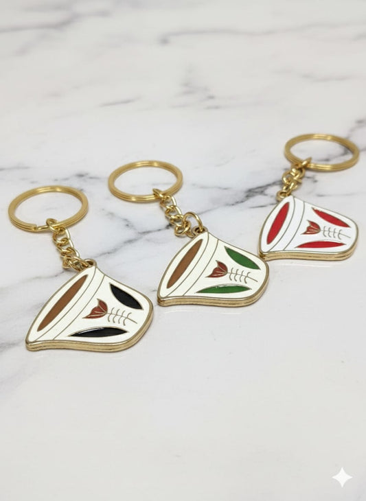 Three decorative keychains with gold chains on a marble surface