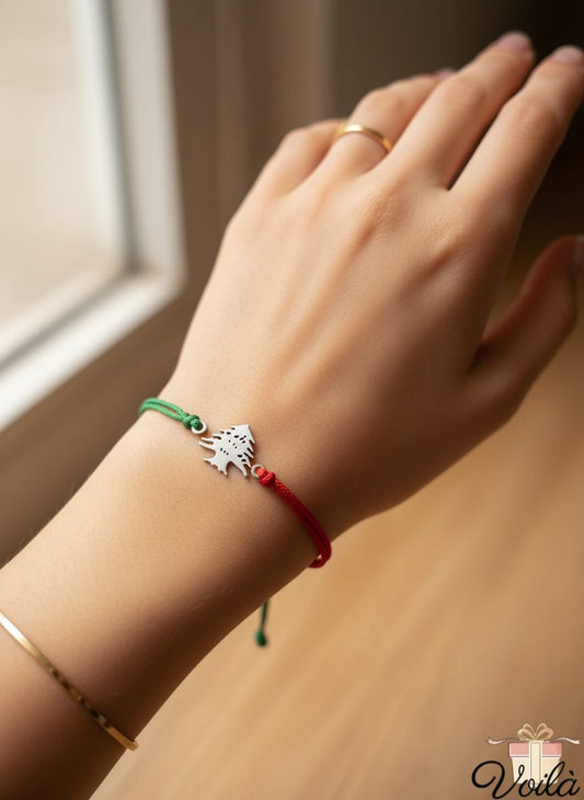 Hand wearing a bracelet with a green and red string, close-up on a wooden surface.