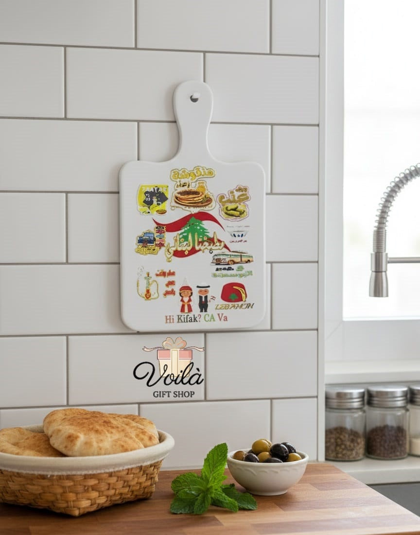 Decorative cutting board with illustrations in a kitchen setting, featuring the Voila Gift Shop logo.