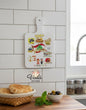 Decorative cutting board with illustrations in a kitchen setting, featuring the Voila Gift Shop logo.
