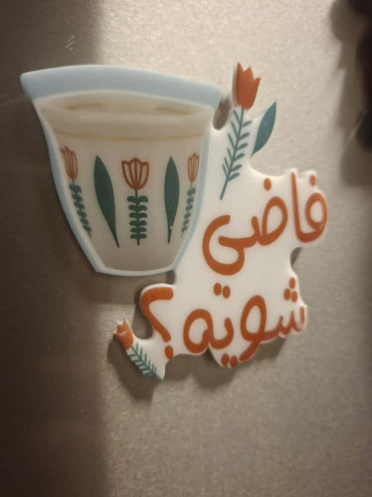Decorative refrigerator magnet with a floral design and Arabic text on a metallic surface.