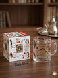 Clear glass mug with decorative design on a wooden table next to its packaging, with 'Voila Liban' branding.