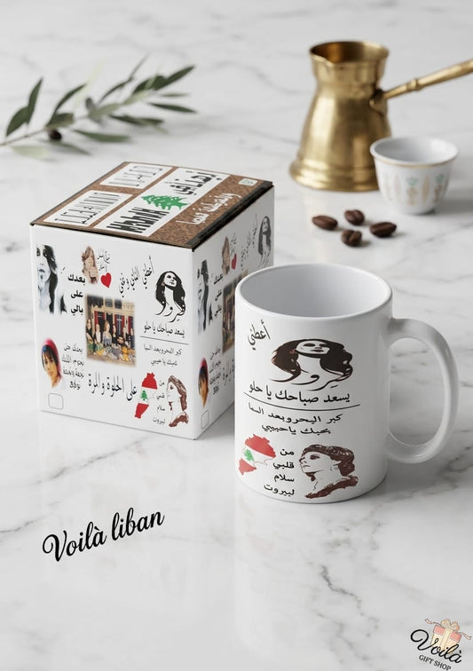 Mug with Arabic text and graphics next to its packaging on a marble surface with coffee beans and a coffee pot.