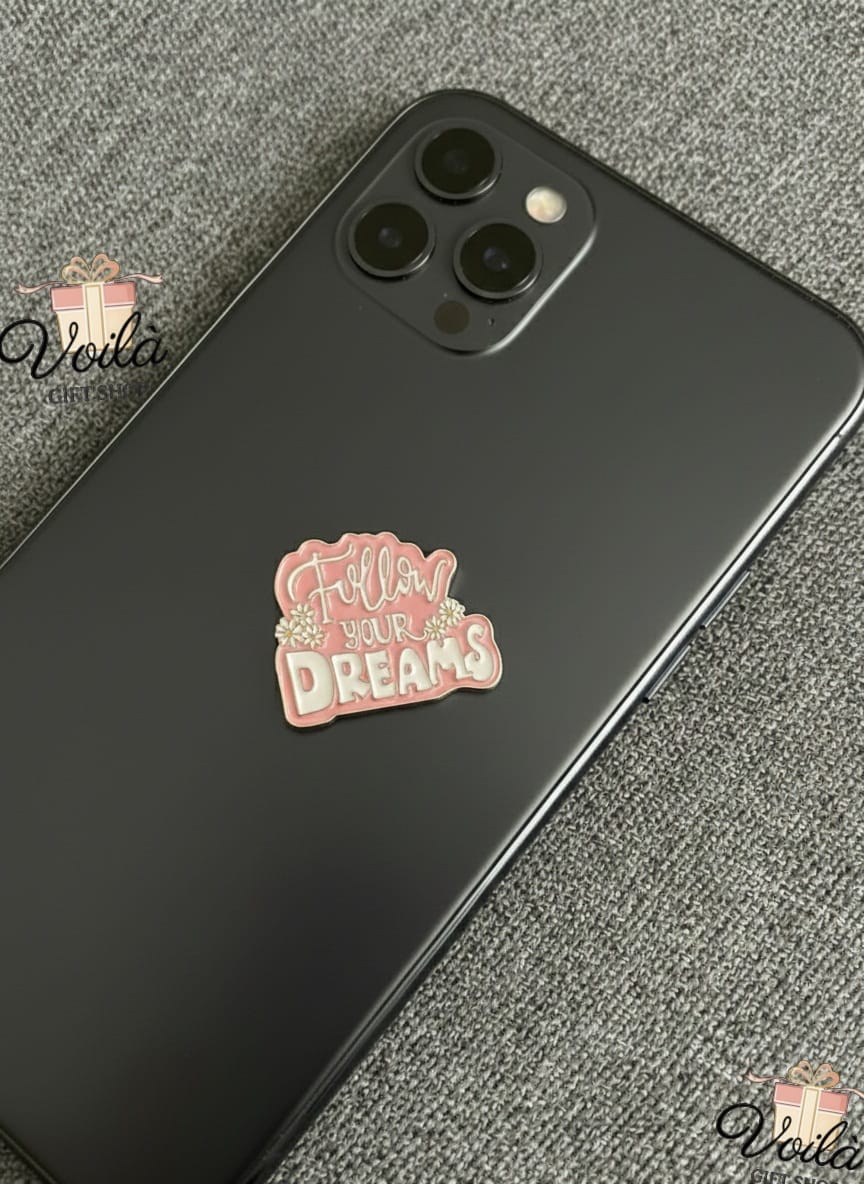 Black phone with a pink 'Follow Your Dreams' sticker on a gray textured surface