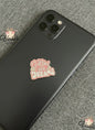 Black phone with a pink 'Follow Your Dreams' sticker on a gray textured surface
