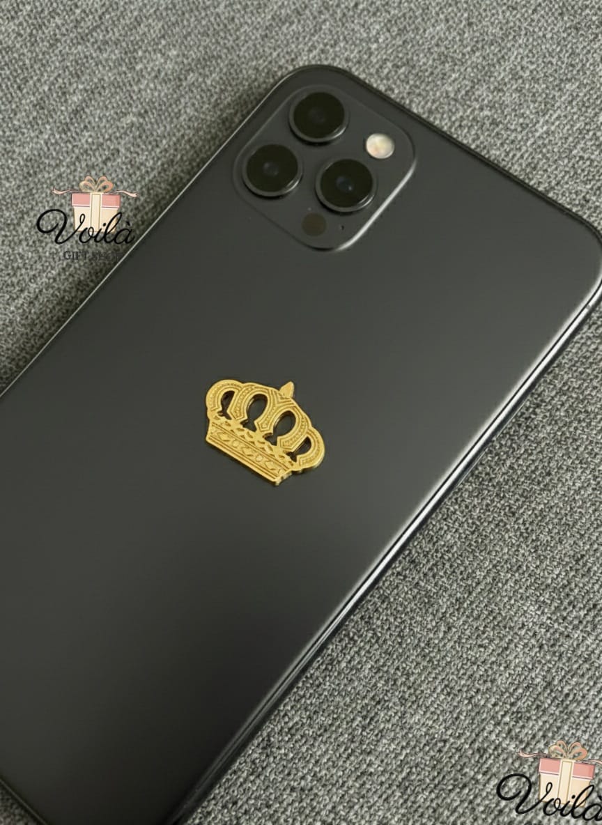 Black smartphone with a gold crown emblem on a gray textured surface, branded 'Veila'.