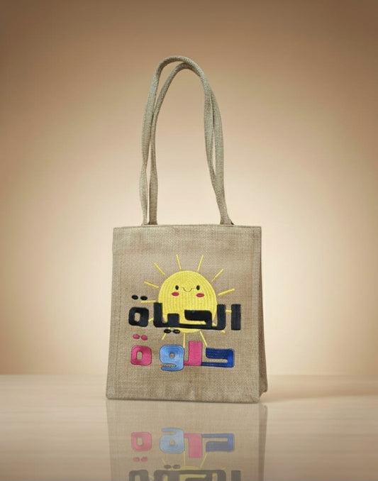 Tote bag with a sun design and text on a reflective surface with a beige background