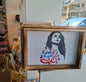 Framed artwork with a stylized portrait and Arabic text on a stand in a store setting.