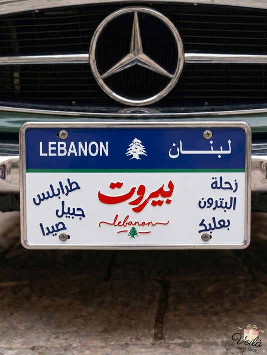 Decorative Lebanese license plate mounted on a classic car, featuring the names of iconic cities in Arabic calligraphy including Beirut in bold red, surrounded by Tripoli, Byblos, Sidon, Zahle, Batroun, and Baalbek.
