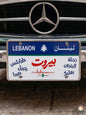 Decorative Lebanese license plate mounted on a classic car, featuring the names of iconic cities in Arabic calligraphy including Beirut in bold red, surrounded by Tripoli, Byblos, Sidon, Zahle, Batroun, and Baalbek.