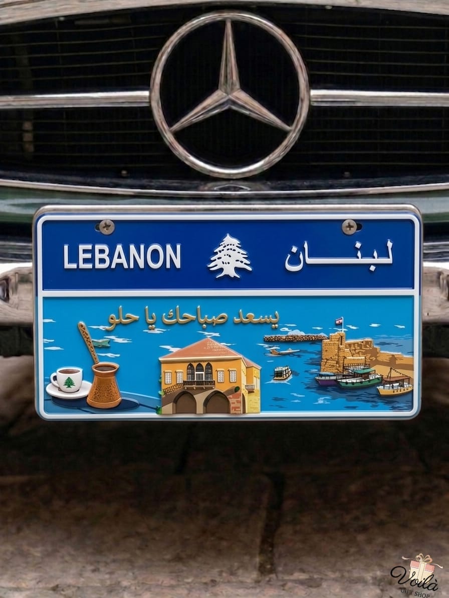 Decorative blue Lebanese license plate mounted on a classic car, featuring a bright coastal scene with the Saida Sea Castle, a traditional stone house, a coffee rakwe, and the Arabic phrase Yis'ed sabahak ya helo.