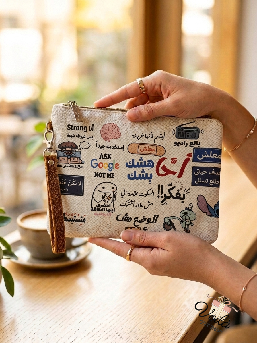 Hands holding a canvas pouch featuring funny Arabic pop culture memes and a brown wristlet strap